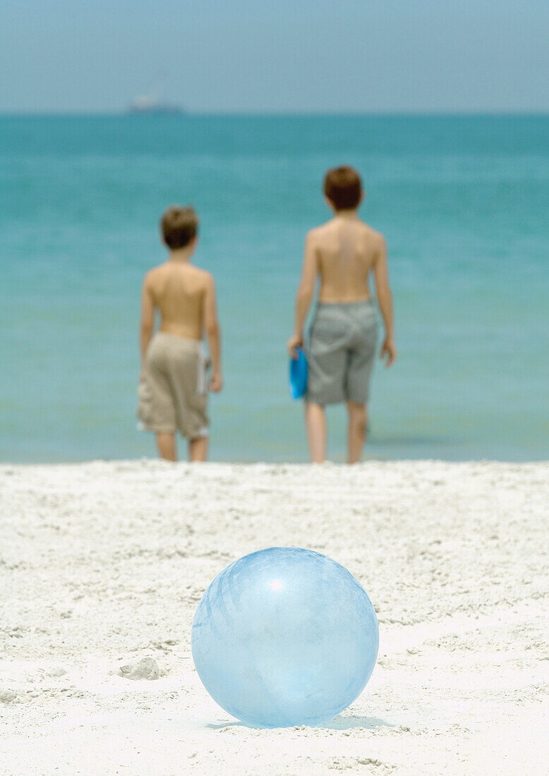 Boys standing near surf, ball in foreground