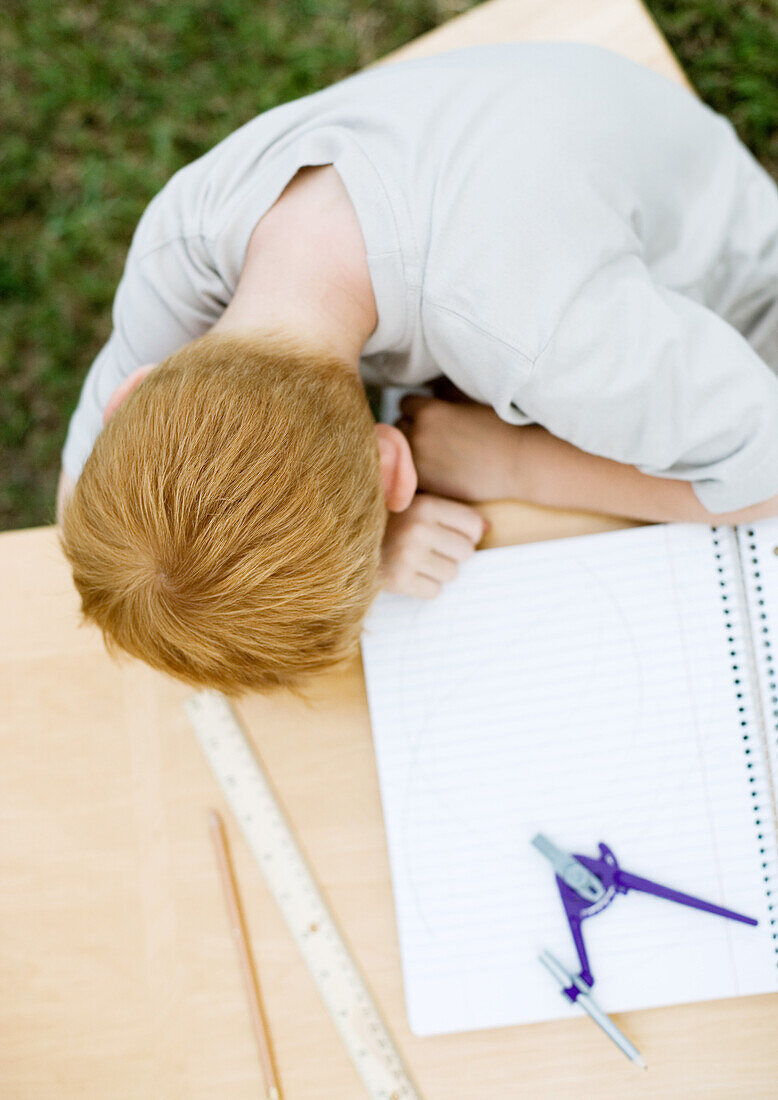 Boy with head on table next to open notebook