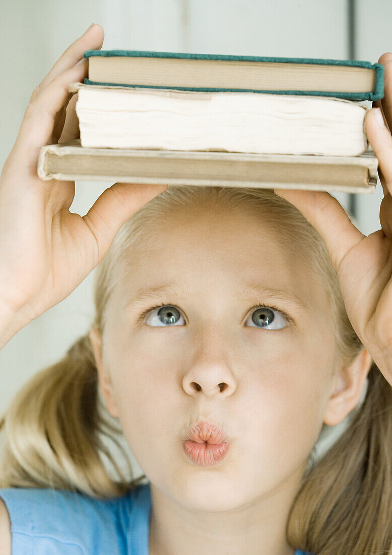 Girl holding stack of books on head, crossing eyes