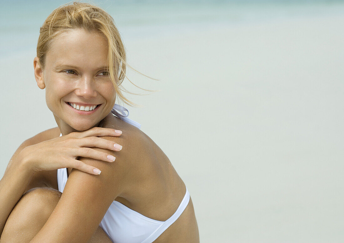 Woman in bikini sitting on beach with hand on shoulder