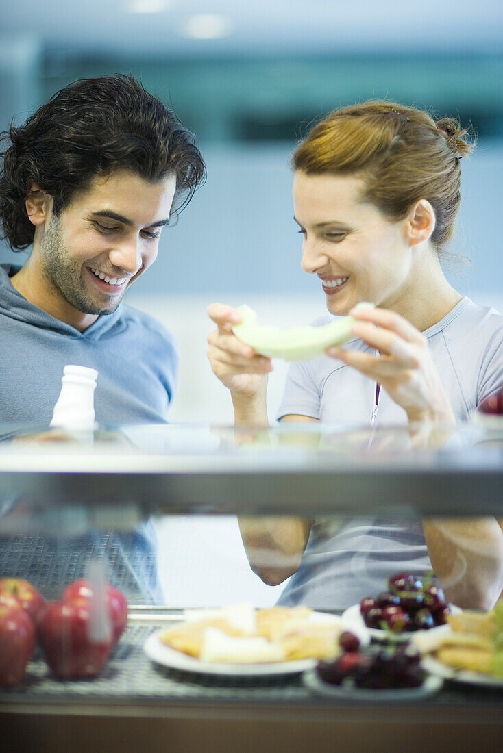 Two young adults standing, having healthy snack in cafeteria