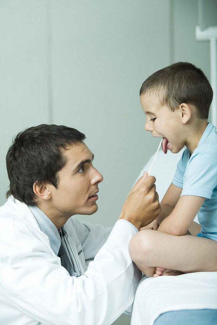 Doctor holding down boy's tongue with tongue depressor