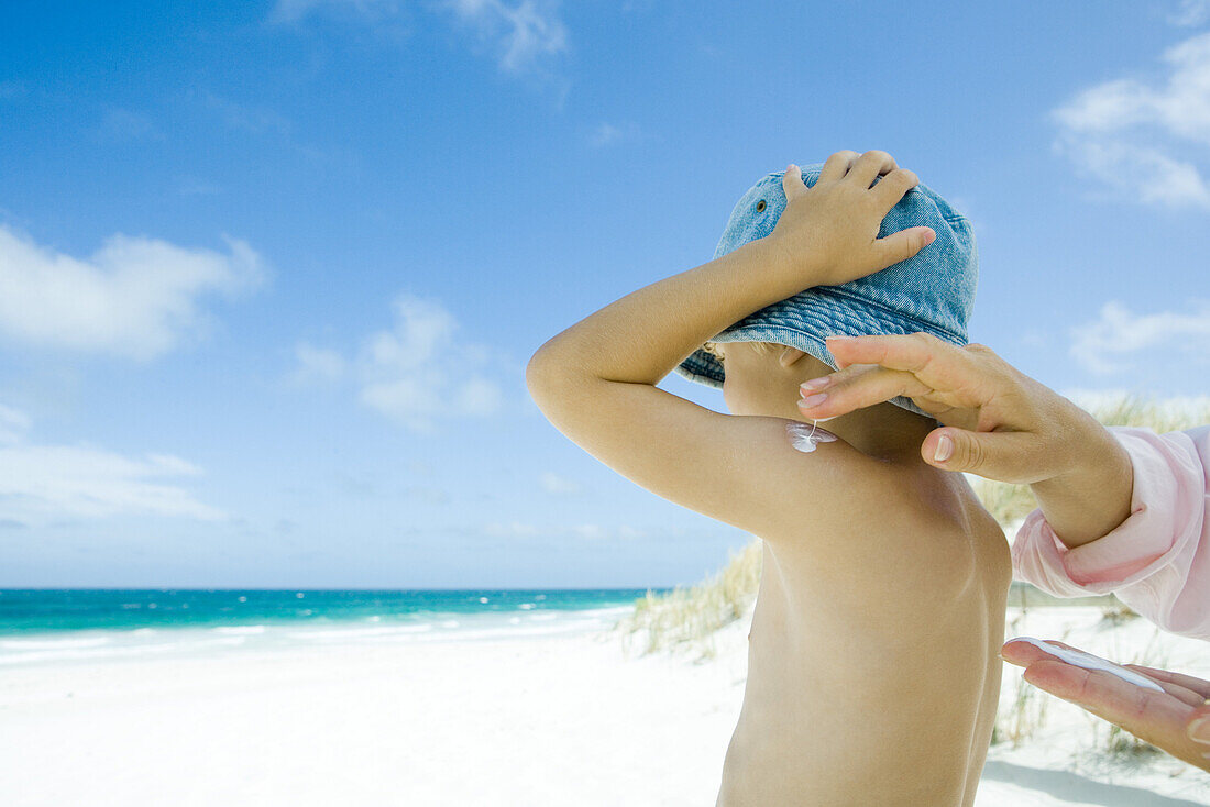 Mother putting sunscreen on child at beach