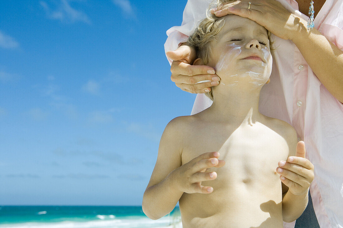 Mother putting sunscreen on child at beach