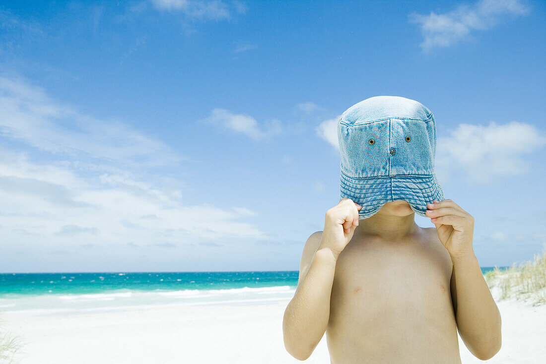Child pulling hat over face at beach