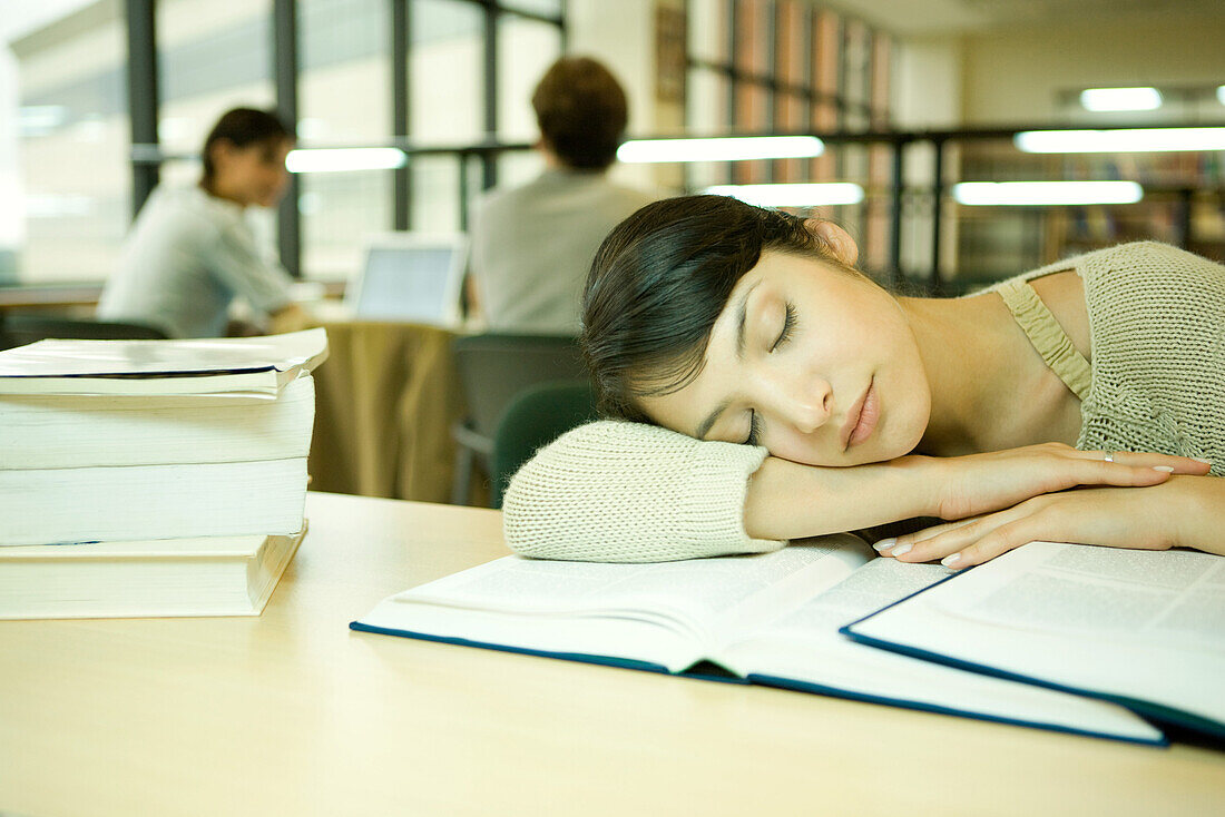 Young woman in university library, head on arm, asleep