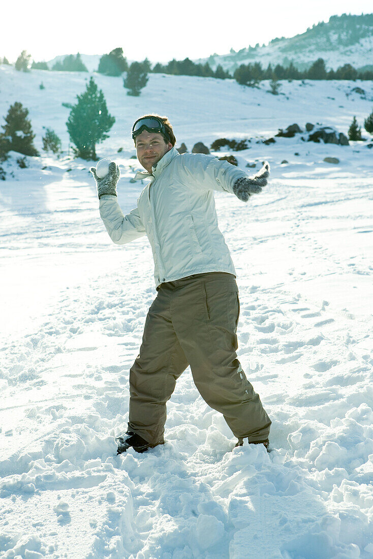 Young man throwing snowball, smiling at camera, full length