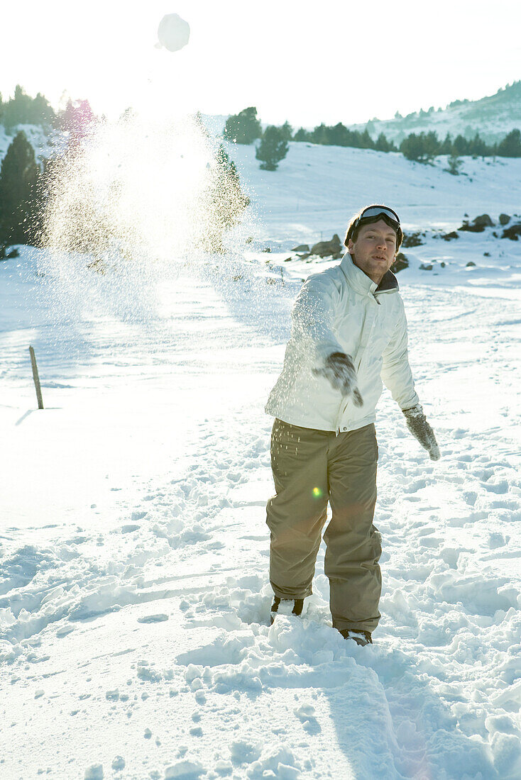 Young man throwing snowball, blurred motion, full length