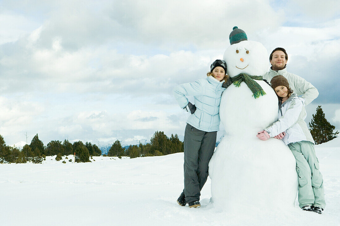 Three young friends leaning against snowman, smiling at camera, portrait