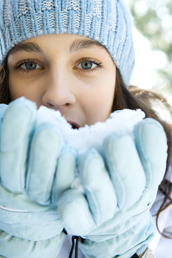 Teenage girl eating snow out of gloved hands, looking at camera, close-up