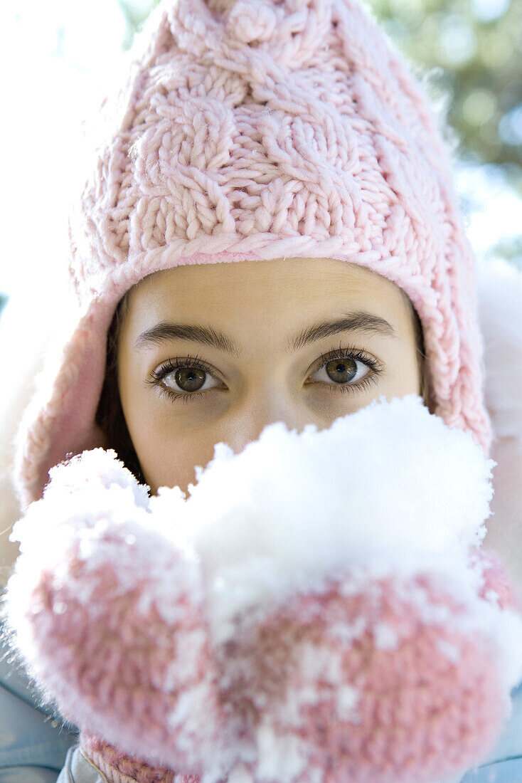 Preteen girl eating snow out of mittened hands, looking at camera