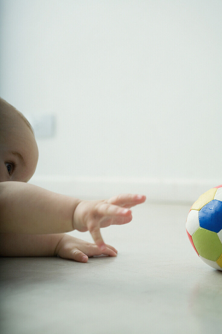 Baby lying on floor, reaching for ball, cropped view