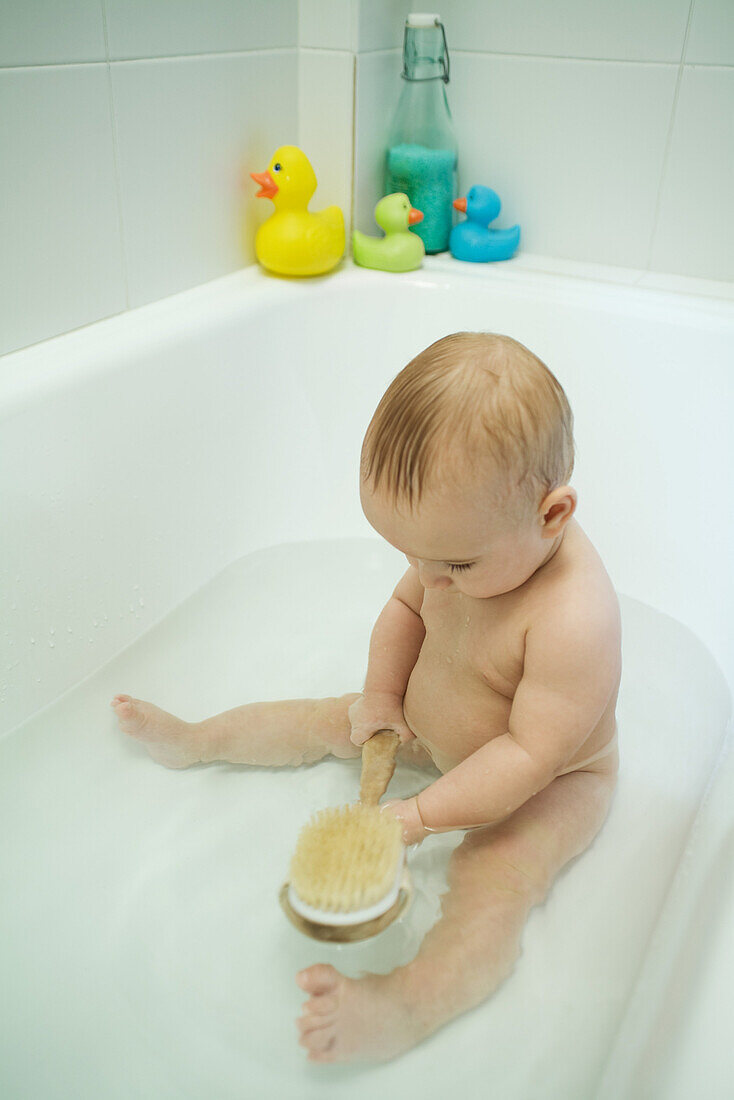 Baby taking bath, holding bath brush, full length