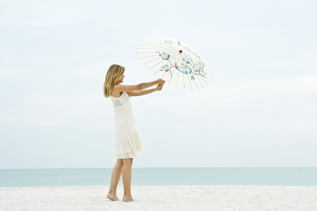 Woman holding parasol on beach, full length