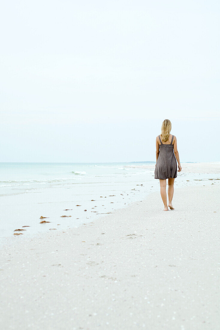 Woman in sundress walking at the beach, rear view