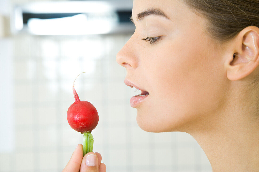 Young woman holding up radish, profile, close-up