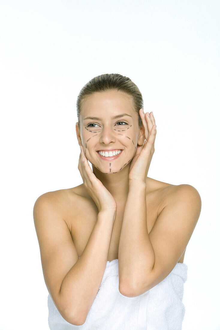 Woman with plastic surgery markings on face, holding head, smiling