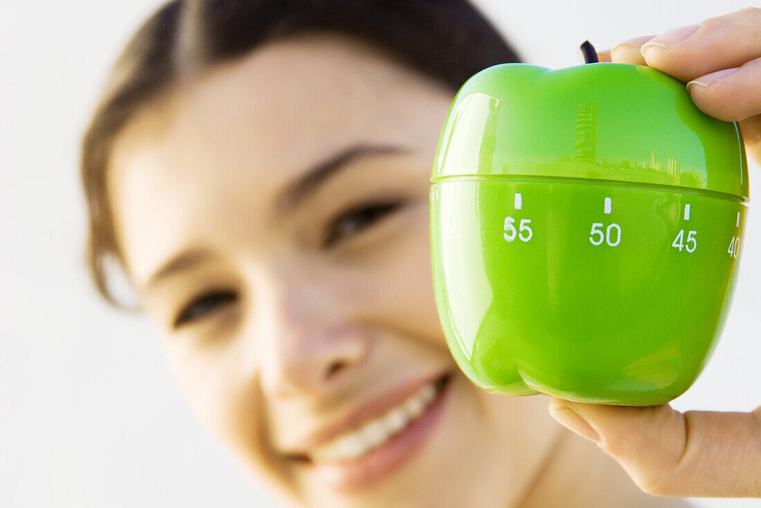 Woman holding up kitchen timer, smiling at camera, focus on foreground