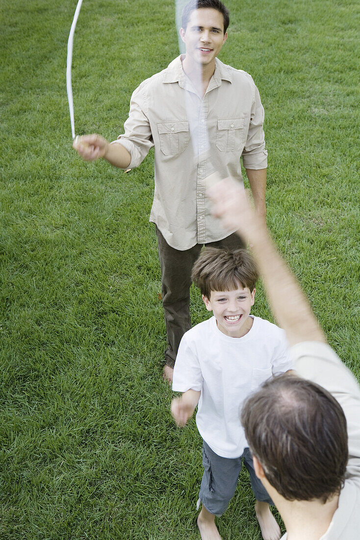 Boy playing jump rope with two men, smiling, cropped view