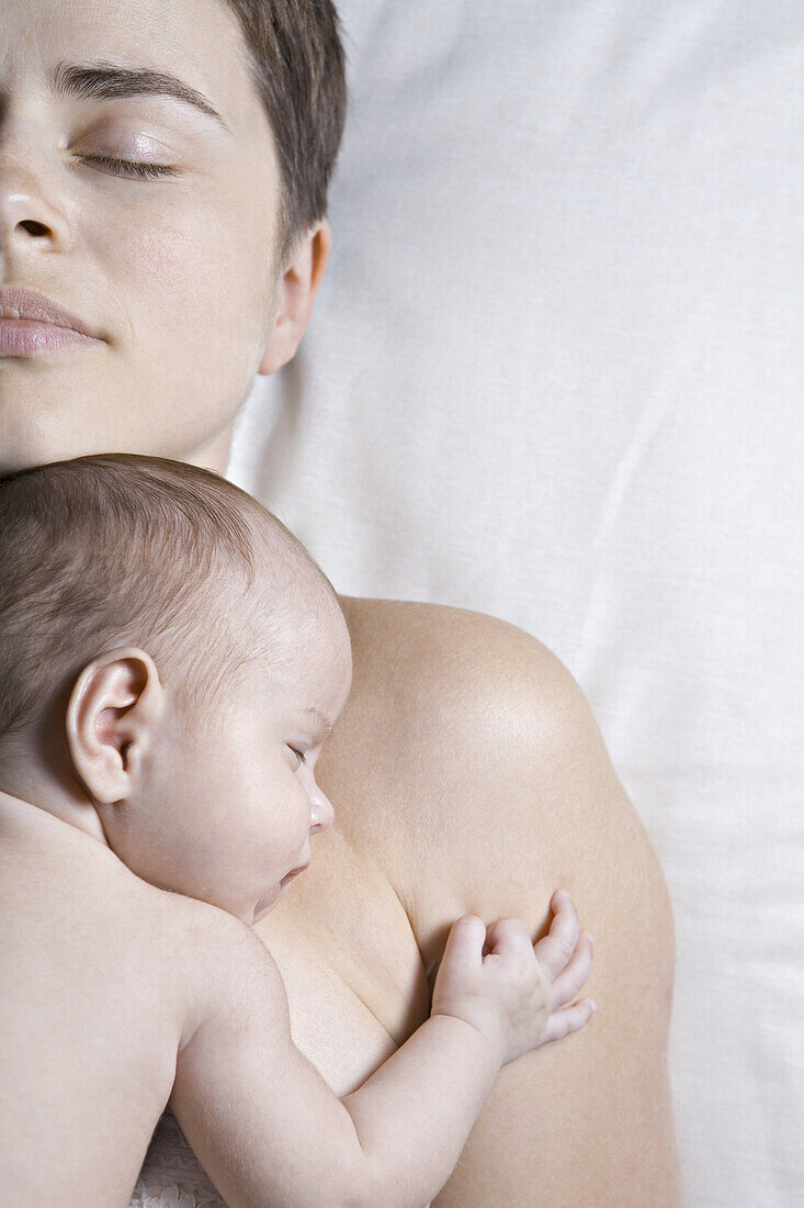 A baby lying on her mother, both sleeping