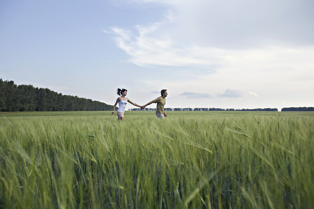 A man and woman holding hands and running through a wheat field