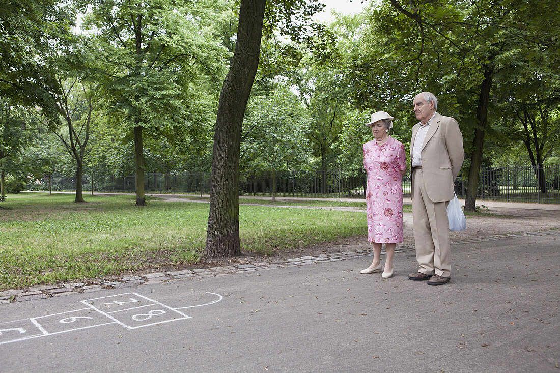 Senior couple contemplate hopscotch in the park