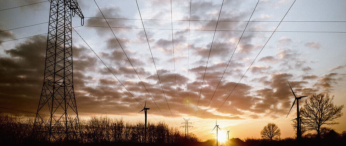 Electricity pylons and wind turbines against cloudy sky at dusk
