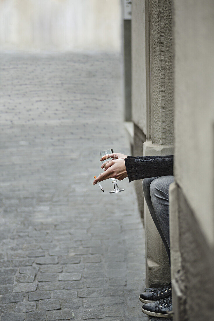 Cropped image of woman holding cigarette and wineglass by sidewalk