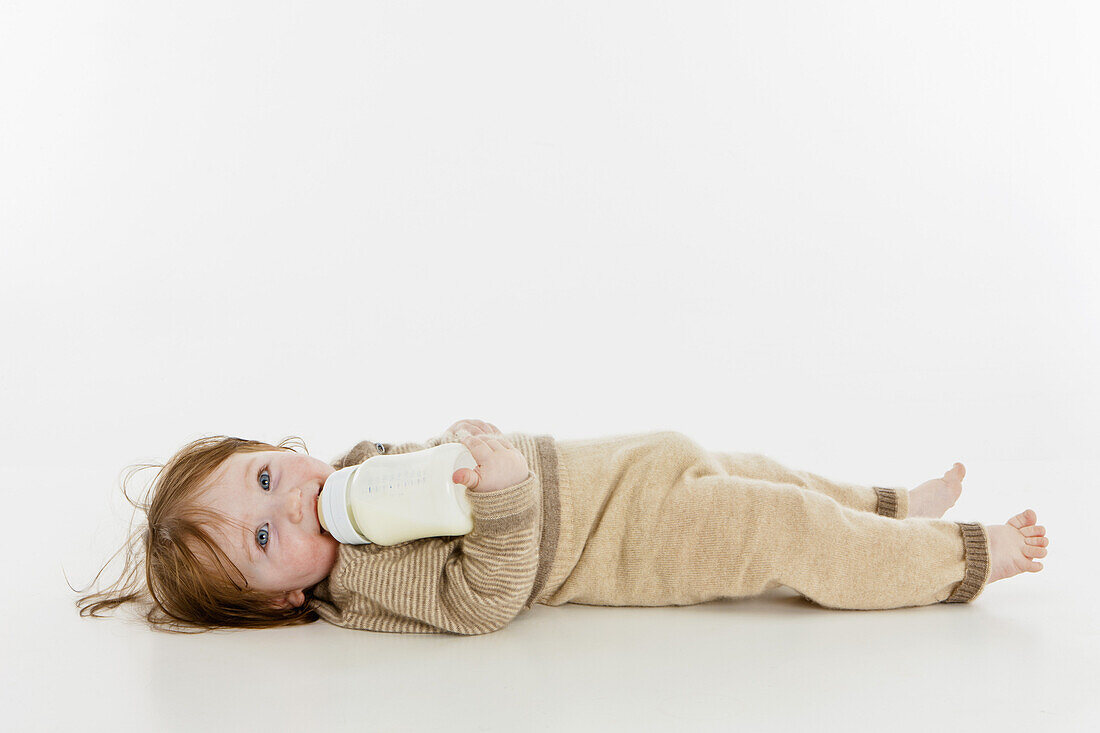 A baby girl lying down with a bottle of milk