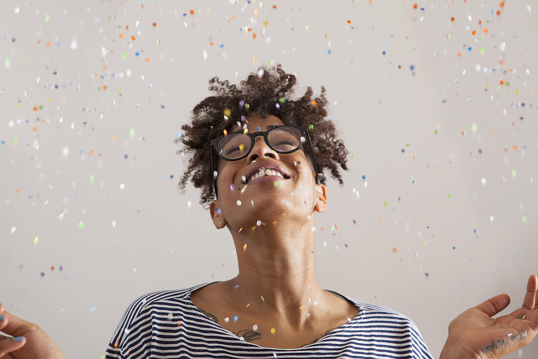 Happy young woman with confetti falling on her over gray background