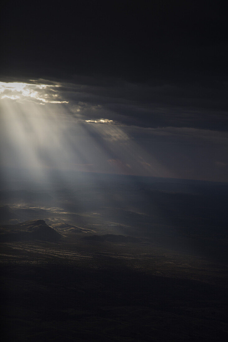 Sun streaming through storm clouds on arid landscape