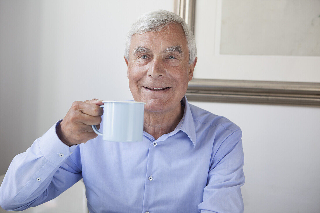 Portrait of happy senior man holding coffee mug at home