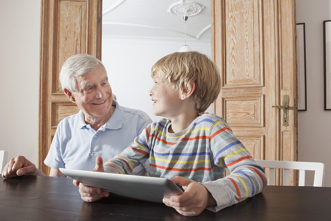 Happy senior man looking at grandson with digital tablet at home