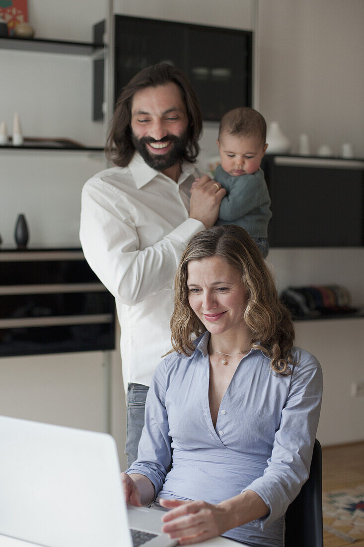 Father with baby girl looking at woman using laptop at home