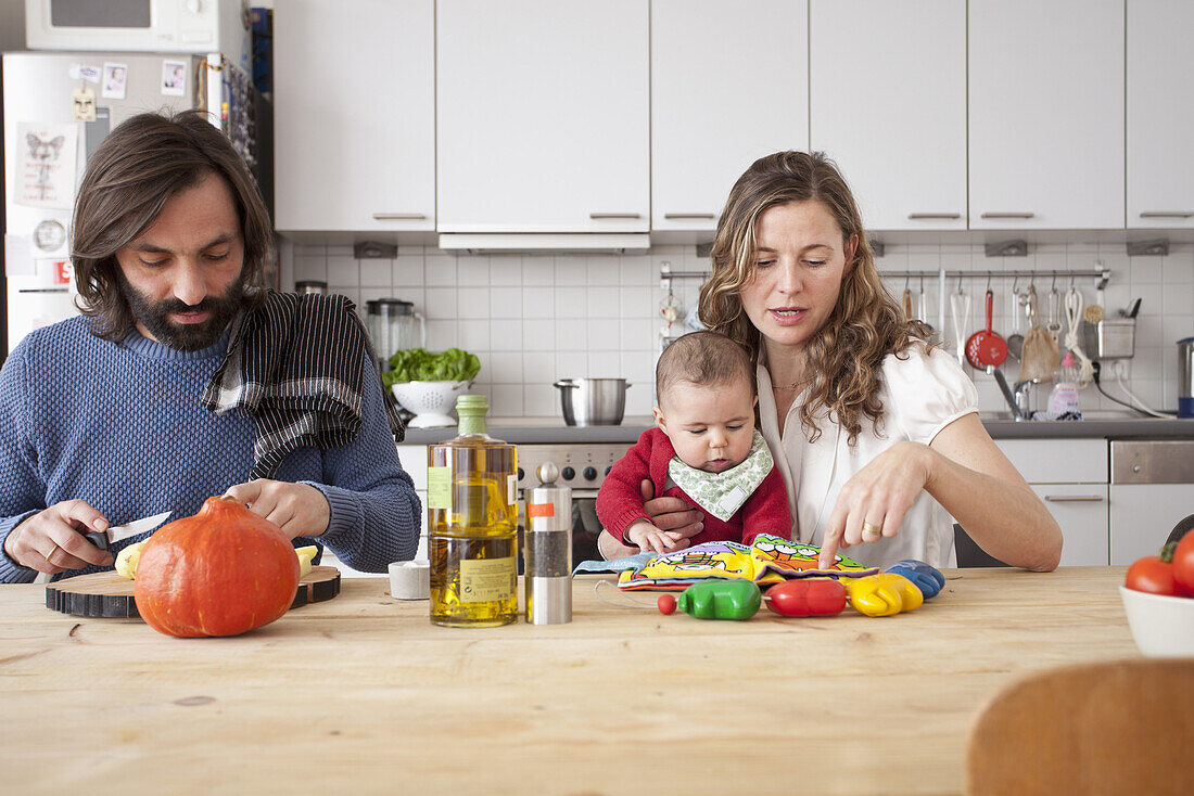 Father cutting vegetables with mother playing with baby girl in kitchen