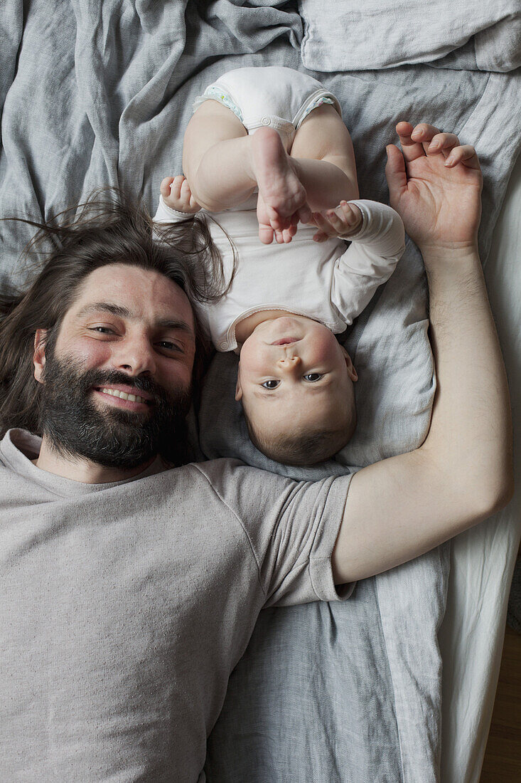 Portrait of smiling father and baby girl lying in bed