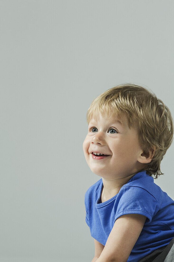 Smiling baby boy looking away over gray background