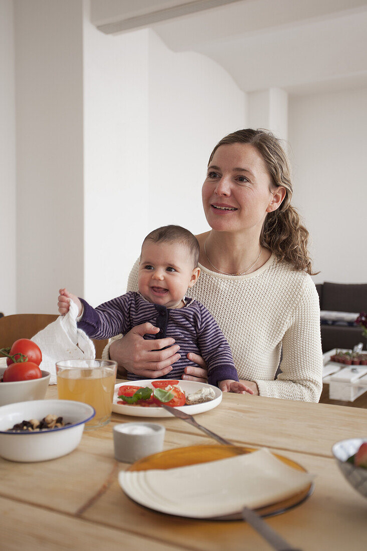 Smiling mother and baby girl looking away while sitting at table