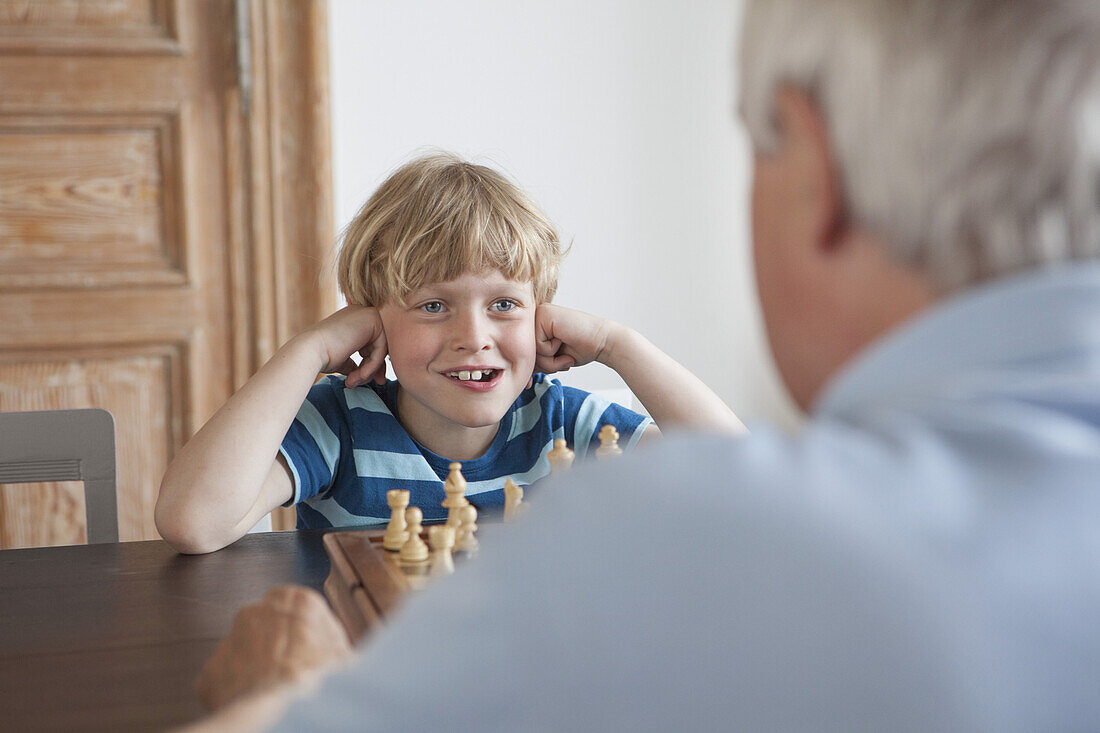 Happy grandson playing chess with grandfather at home