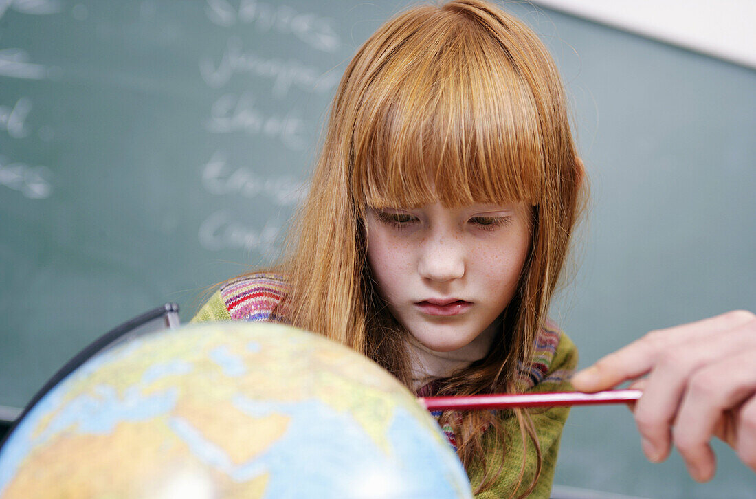 A student looks attentively at a globe with her teacher