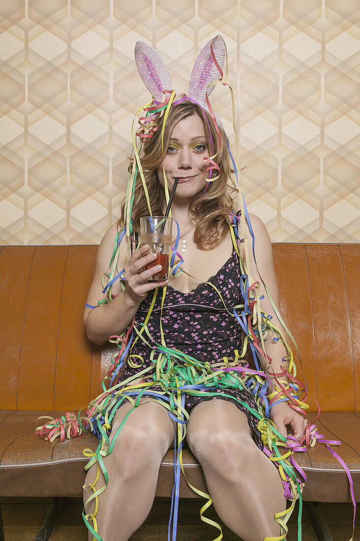 A tipsy woman drinking a cocktail and covered in streamers, portrait