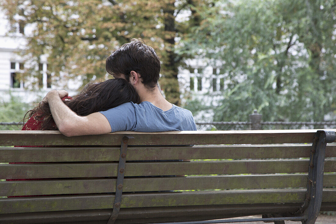 Young couple sitting on park bench, rear view