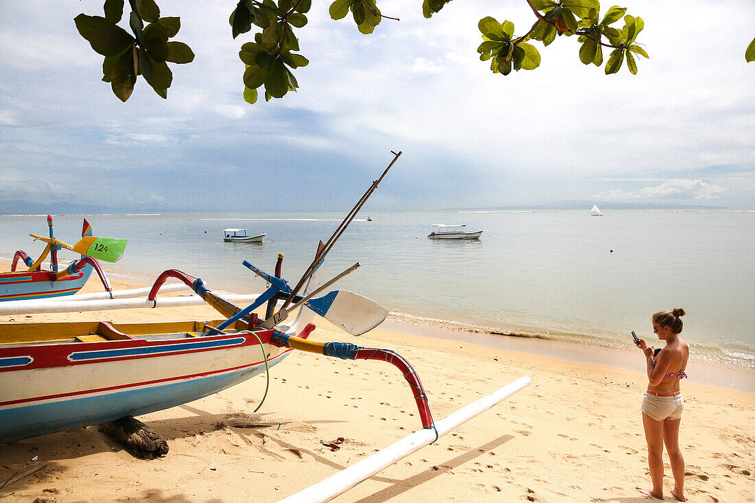 Frau fotografiert traditionelles buntes Fischerboot, Sanur, Denpasar, Bali, Indonesien