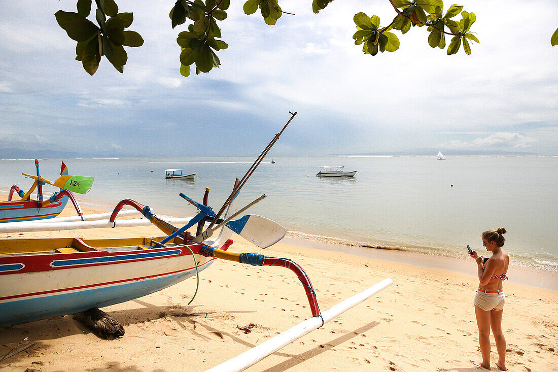 Woman taking pictures of a colorful traditional fishing boat at beach, Sanur, Denpasar, Bali, Indonesia