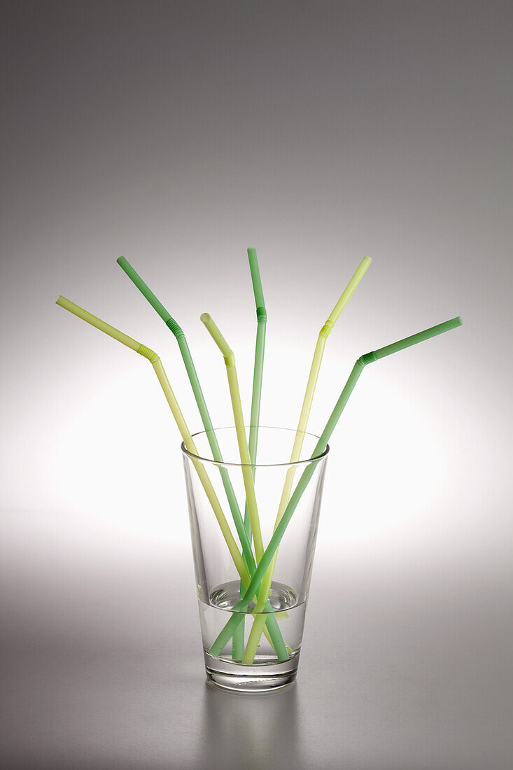 A glass with water in it and three green drinking straws and three yellow ones