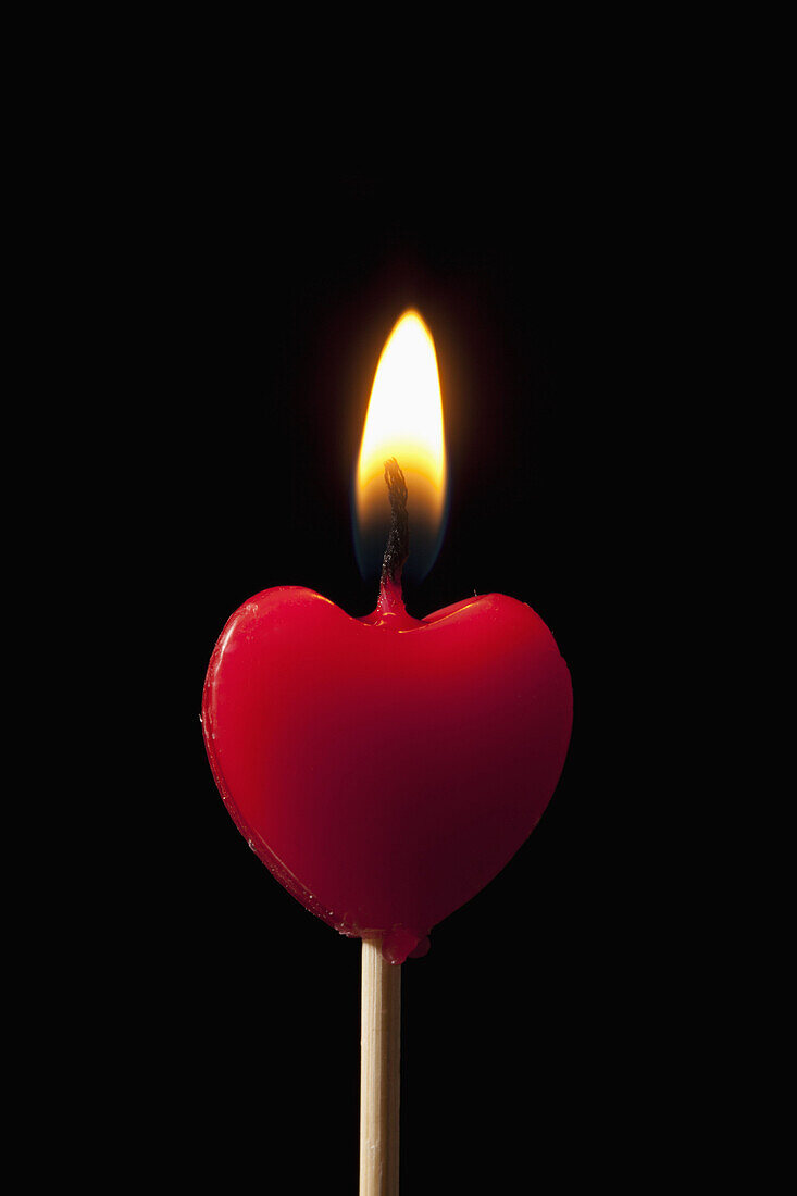 A lit heart shaped candle on a stick