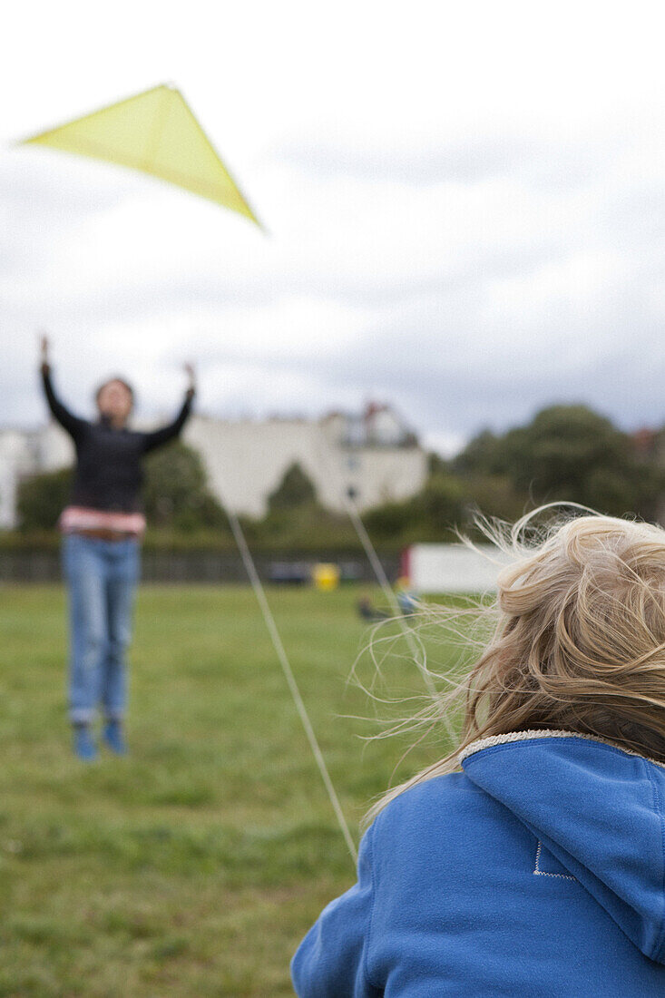 A boy flying a kite with the help of his mother in the background, focus on boy