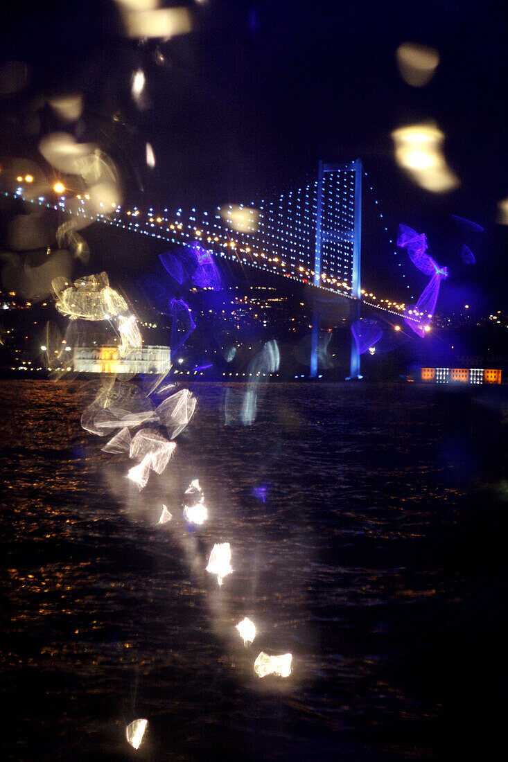 Reflected light and view of an illuminated bridge over water at night, Istanbul, Turkey