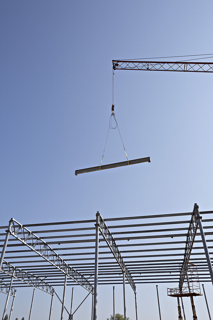 Crane lowering steel beam towards construction frame