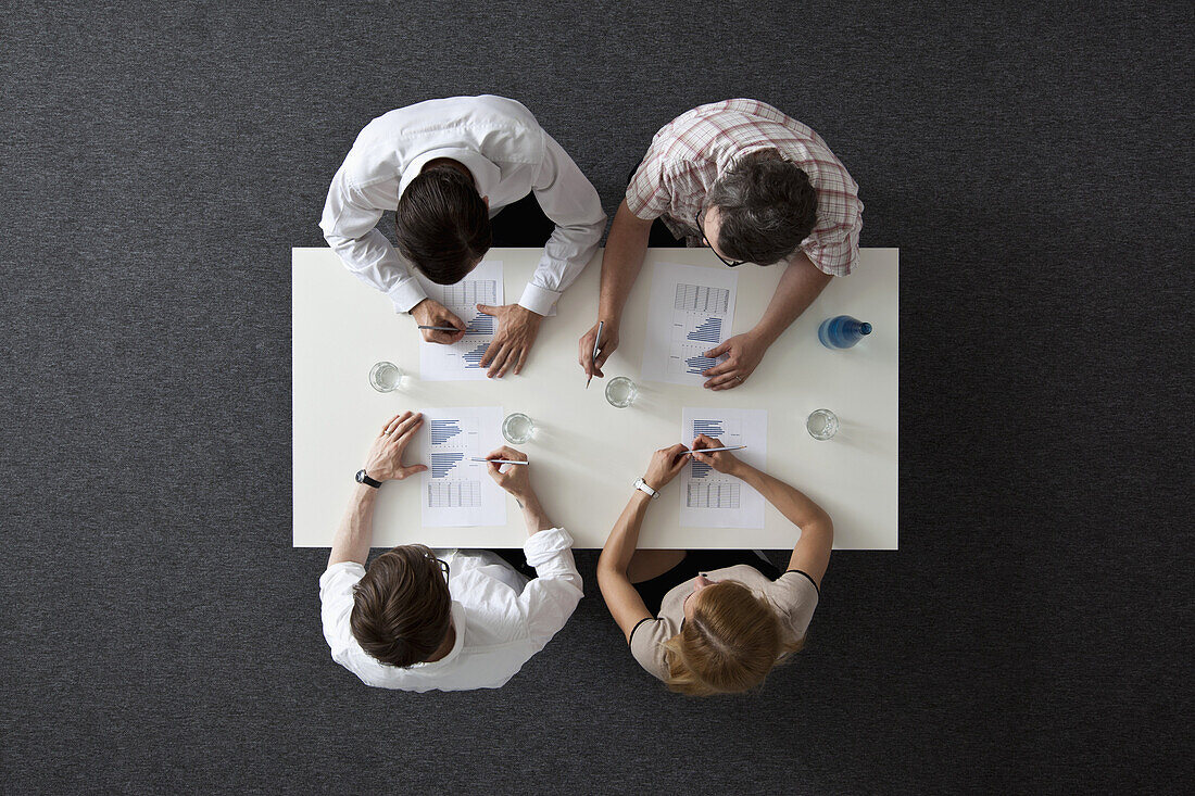 A business meeting with three businessmen and a businesswoman, overhead view